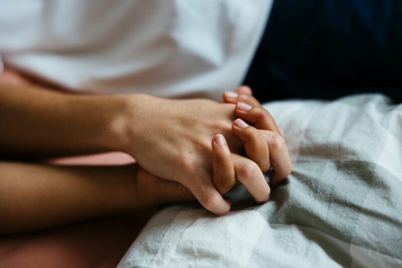 Crop boy and girl holding hands resting in bed